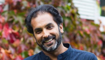 Photo of Jacob Rajan wearing a blue shirt and smiling into the camera