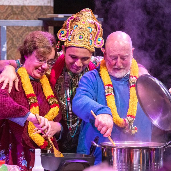Actor Justin Rogers stands between two audience members as they cook rice and dahl