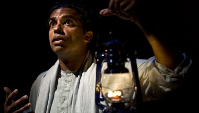 Actor Jacob Rajan stands with a surprised look on his face holding a lantern