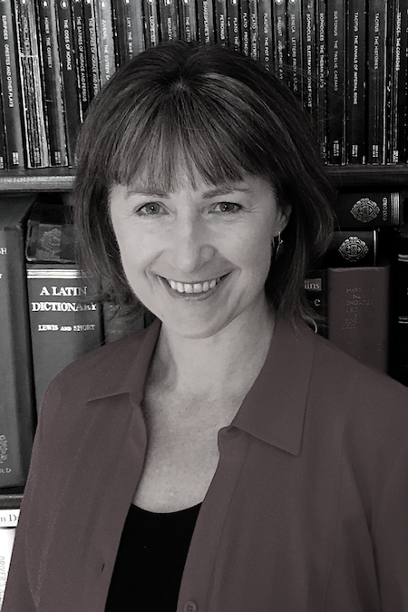Jude Froude smiles in front of a full bookcase. She has short dark hair with a fringe and wears a collared top.