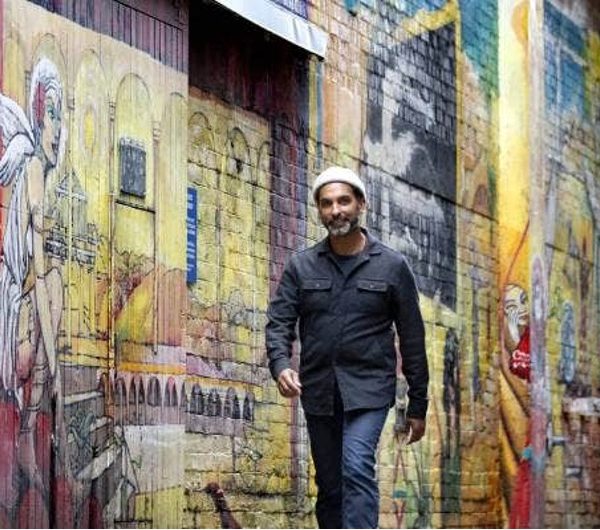 Jacob Rajan walks towards the camera in front of a painted brick wall