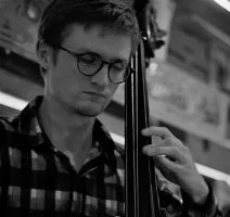 Eamon, a young man with glasses and a collared shirt, closes his eyes as he plays the cello.