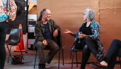 Murray and Elizabeth sit at an event chatting and laughing while holding drinks and food