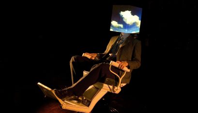 Actor sits in a dentist chair with a square box on his head. the box shows a sky with clouds on it