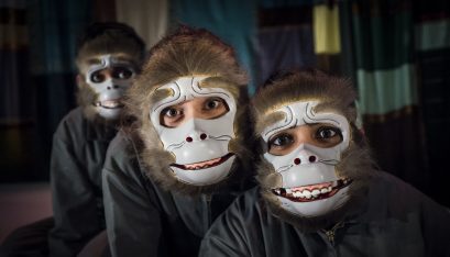Three actors look into the camera wearing monkey maks