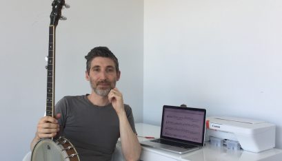 David Ward sits in front of his desk holding a banjo on his knee