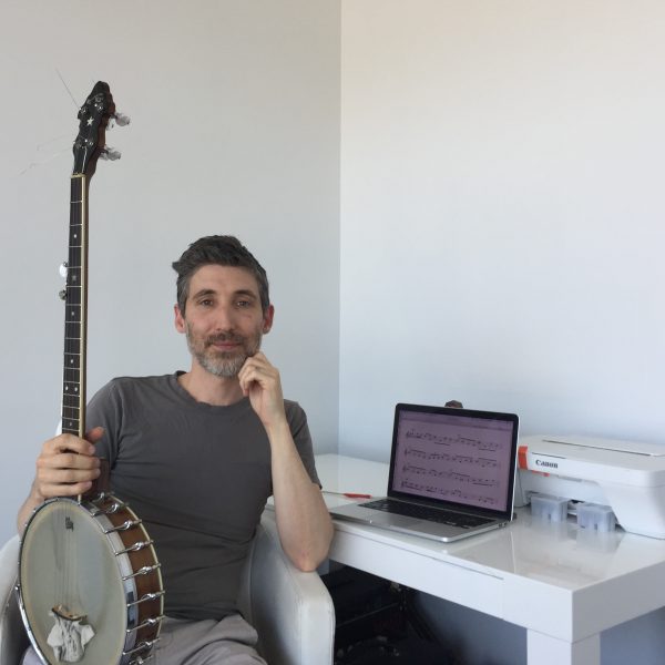 David Ward sits in front of his desk holding a banjo on his knee