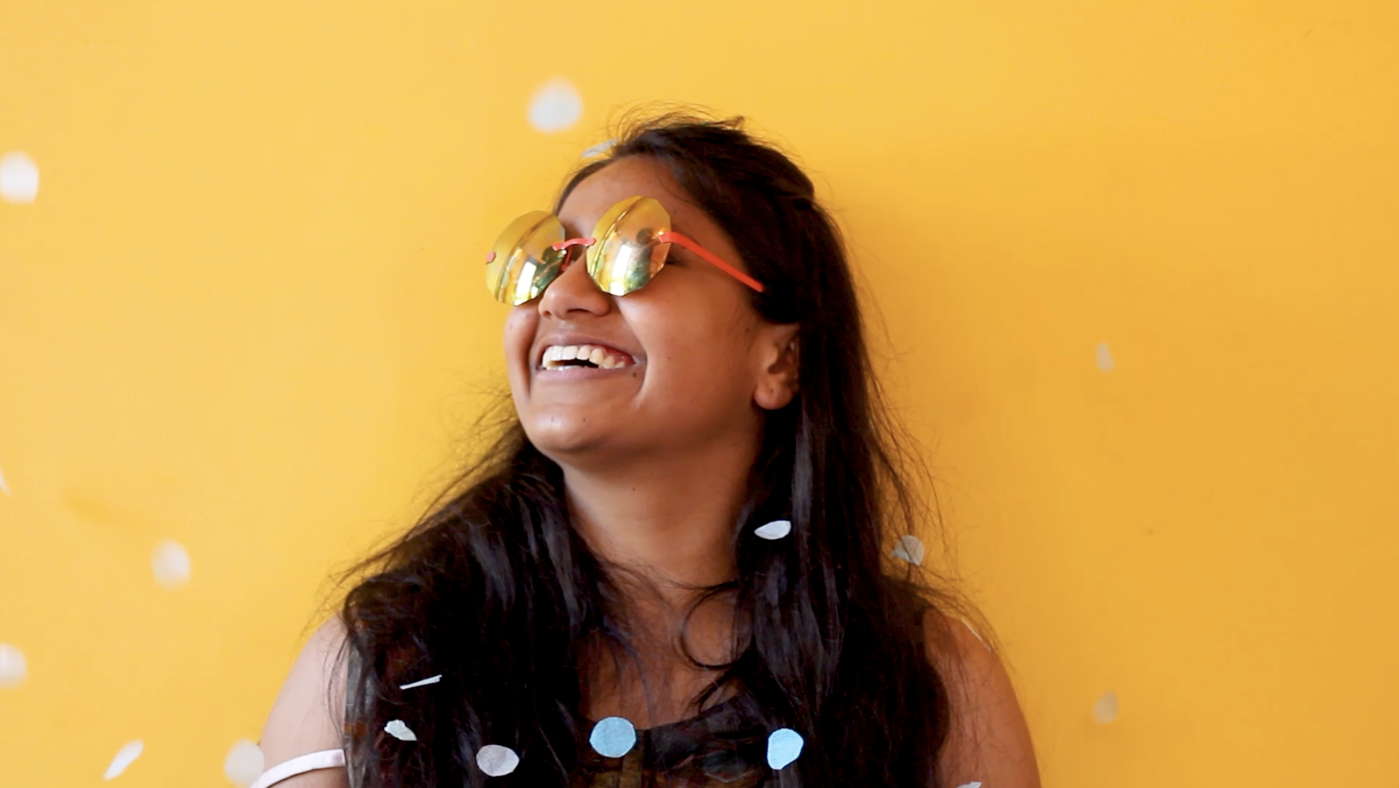Actor Kalyani smiles past the camera in a black shirt and sunglasses. Behind him is a yellow wall.