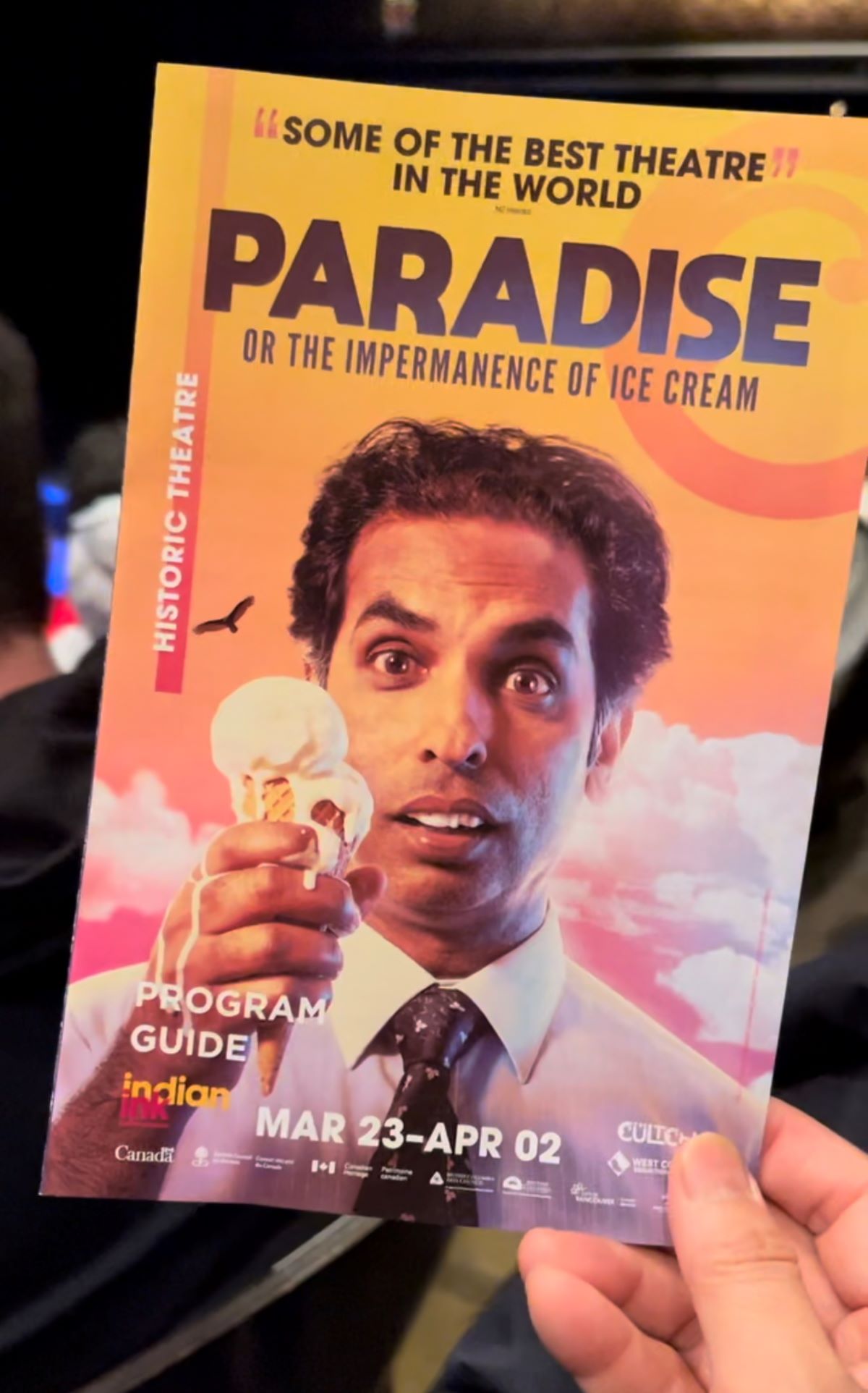 Someone holds a Paradise programme from The Cultch in Canada. It shows Actor Jacob Rajan holds a melting ice cream with the title of the play
