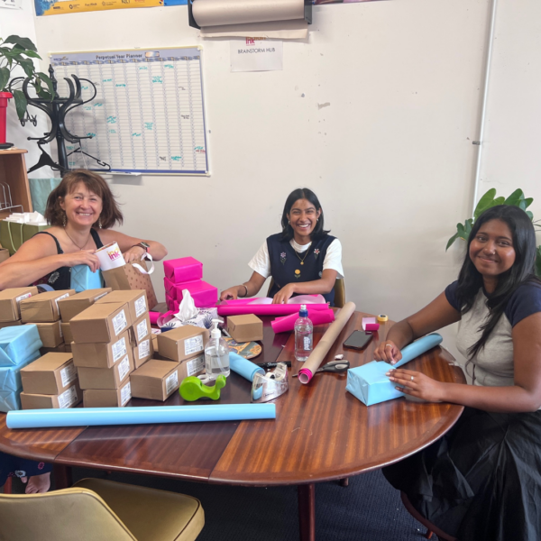 Jude, Reethi & Shreya sit around the INK table wrapping parcels