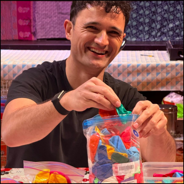Justin Rogers sitting at a table laughing at the camera while packing a bag of balloons