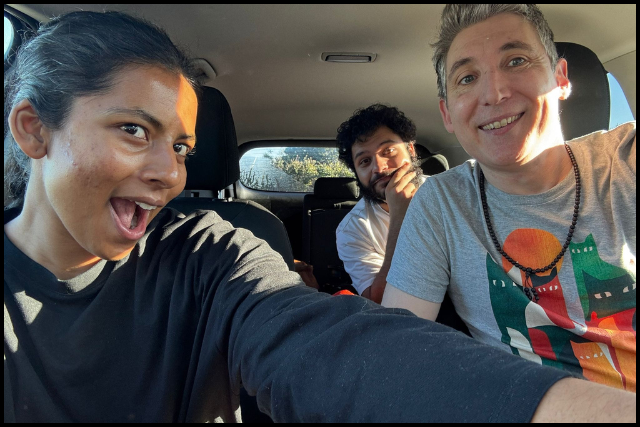 Dave sits on Drivers side (right) smiling at the camera. Alisha sits on the left holding the camera in a selfie position. Jehangir is in the backseat. 