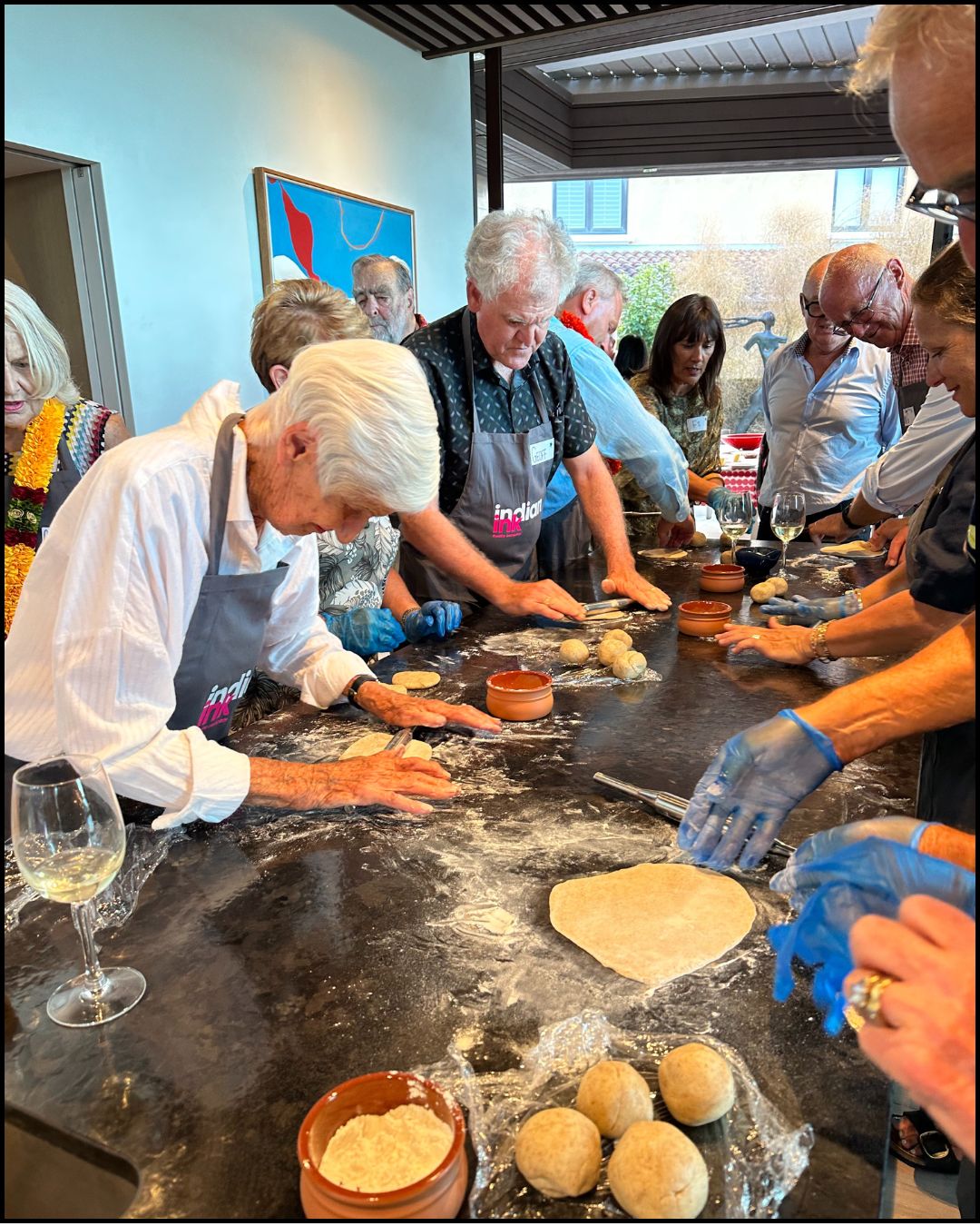 Adults gathered around a kitchen island rolling dough and shaping flatbreads during a hands-on cooking class.