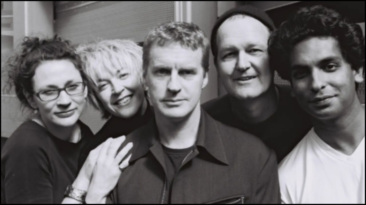 Black-and-white portrait of five adults closely grouped—two women and three men, most smiling while one man looks neutral.
