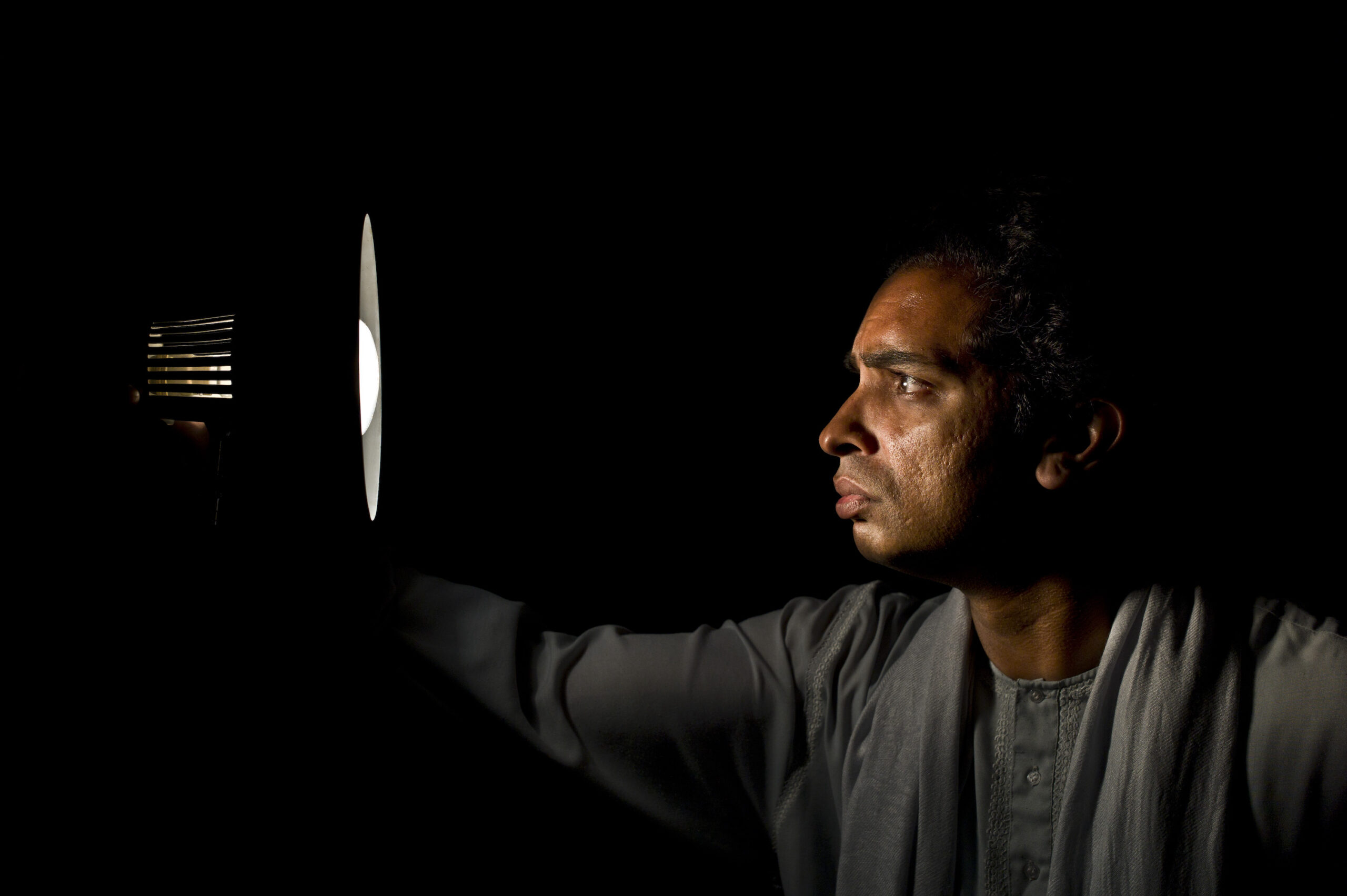 Man in profile staring at a round lamp, his face illuminated against a black background.